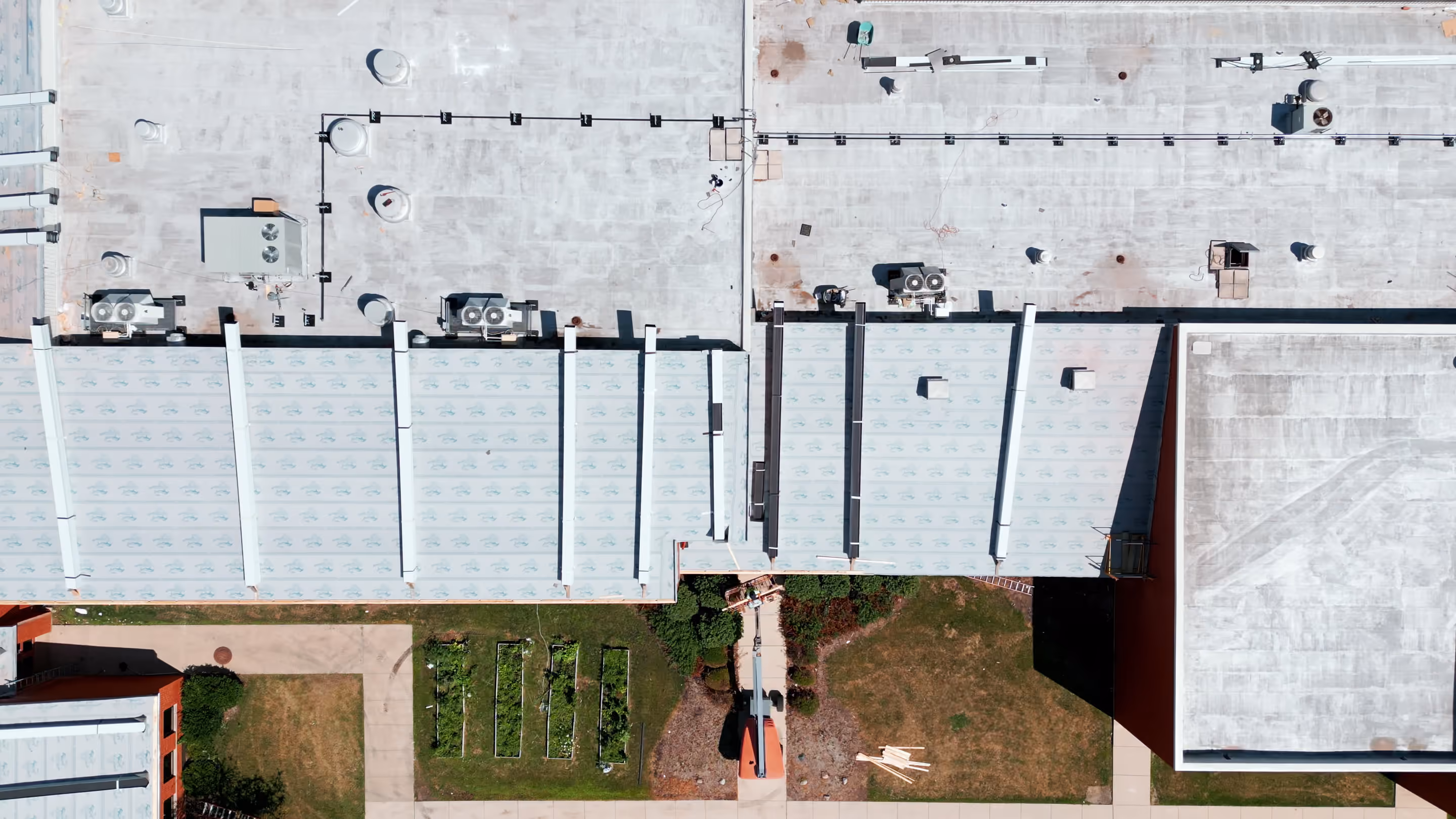 Large flat commercial roofs seen from directly above, with air-conditioning units and vents on a gray flat roof and a long pitched roof section beside it